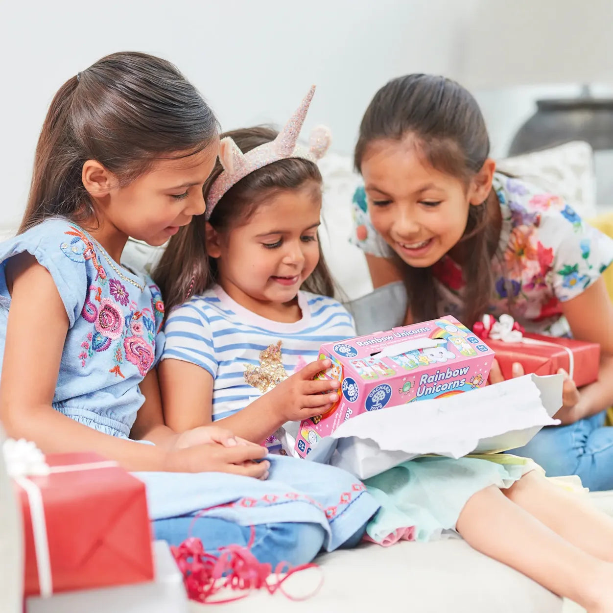 Three young girls opening a 'Rainbow Unicorns' toy box together.