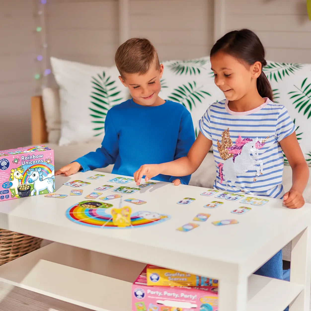 Two children playing with a board game at a table, surrounded by colorful game boxes.