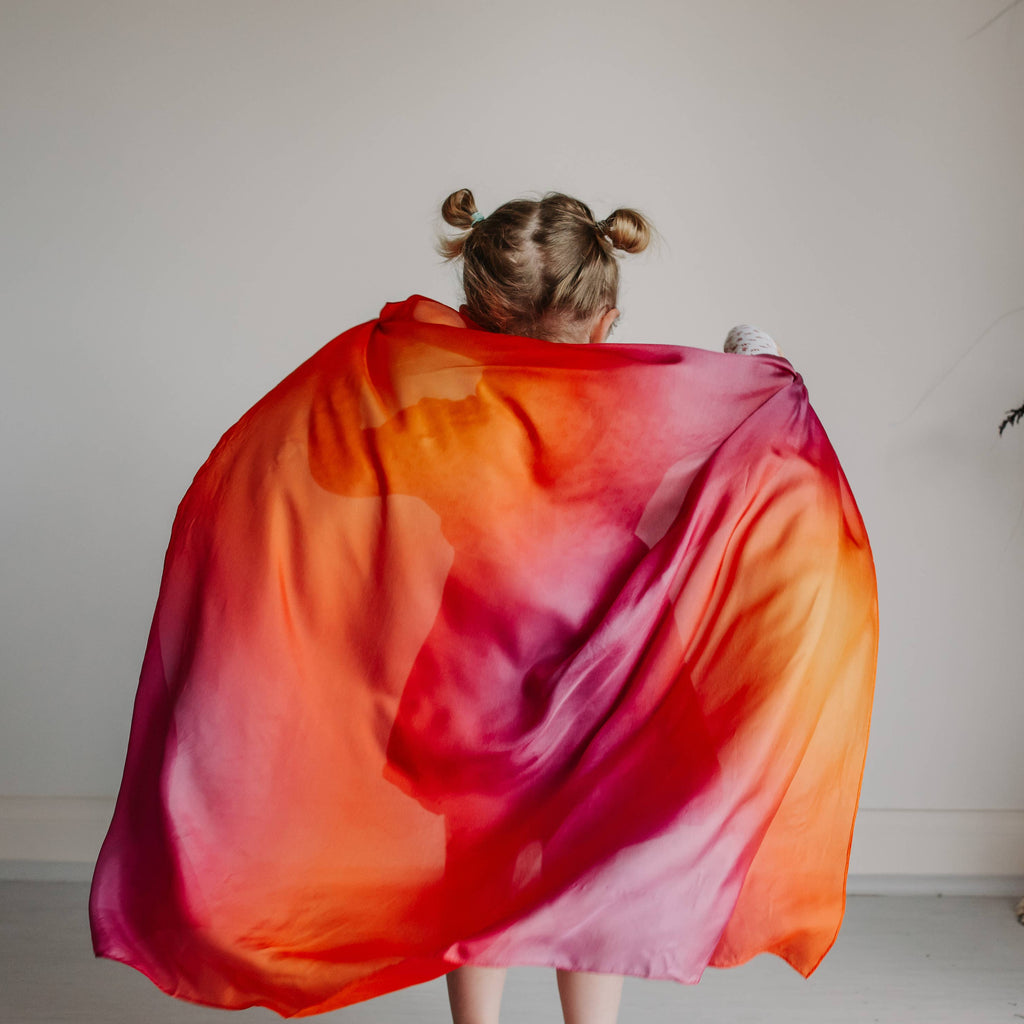 Person holding a colorful scarf in front of a plain wall with decorative elements.