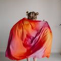 Person holding a colorful scarf in front of a plain wall with decorative elements.