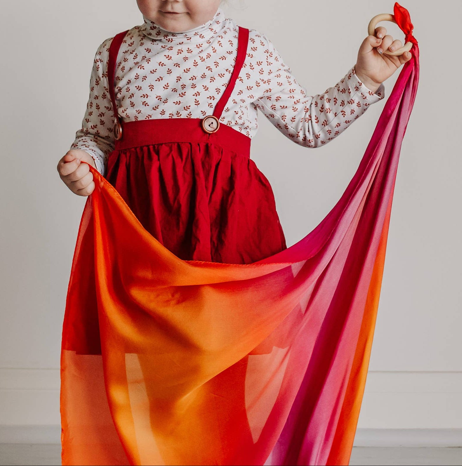 Child in a red dress holding a colorful fabric against a neutral background