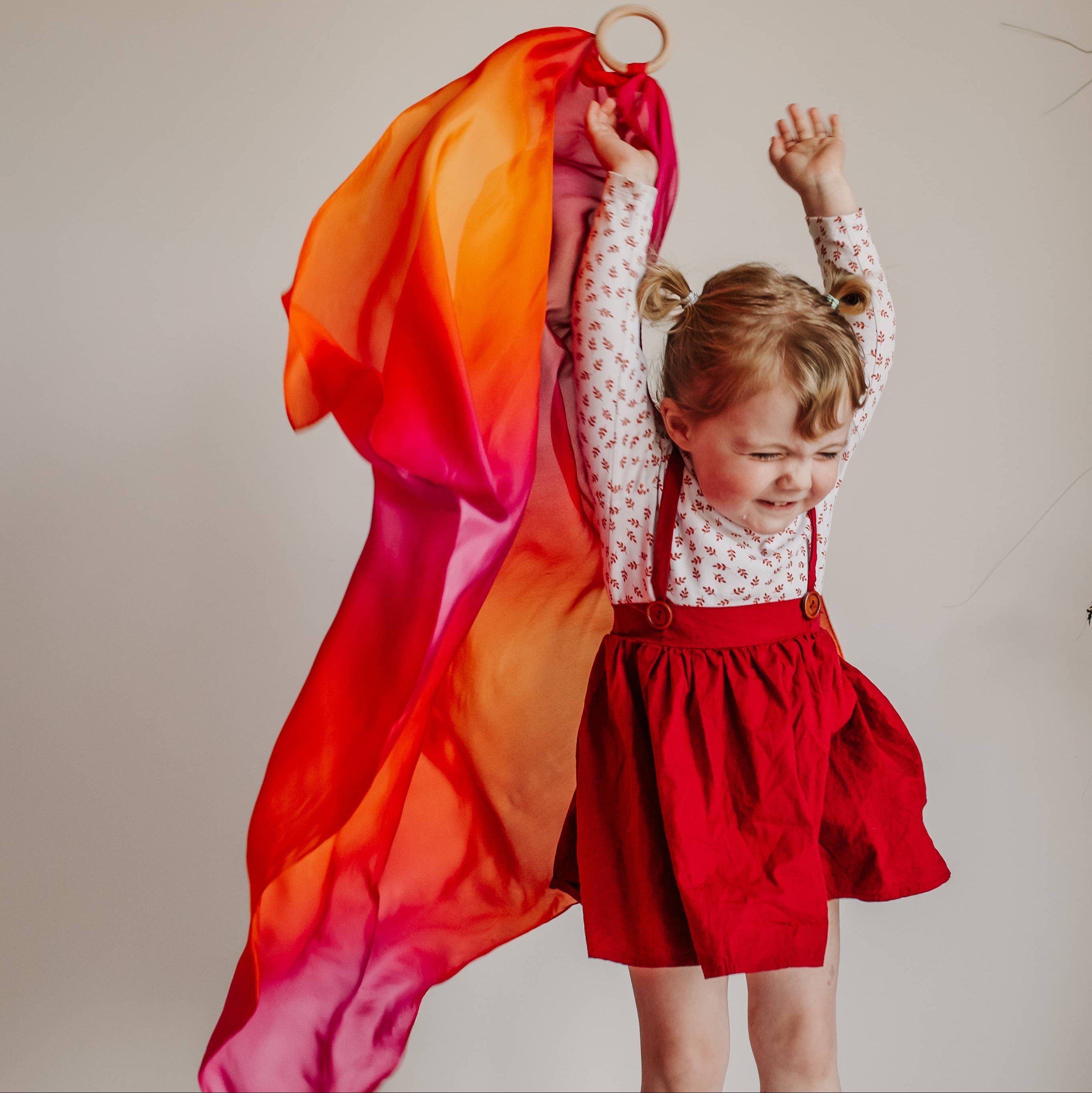 Child in a red dress holding a colorful fabric against a neutral background