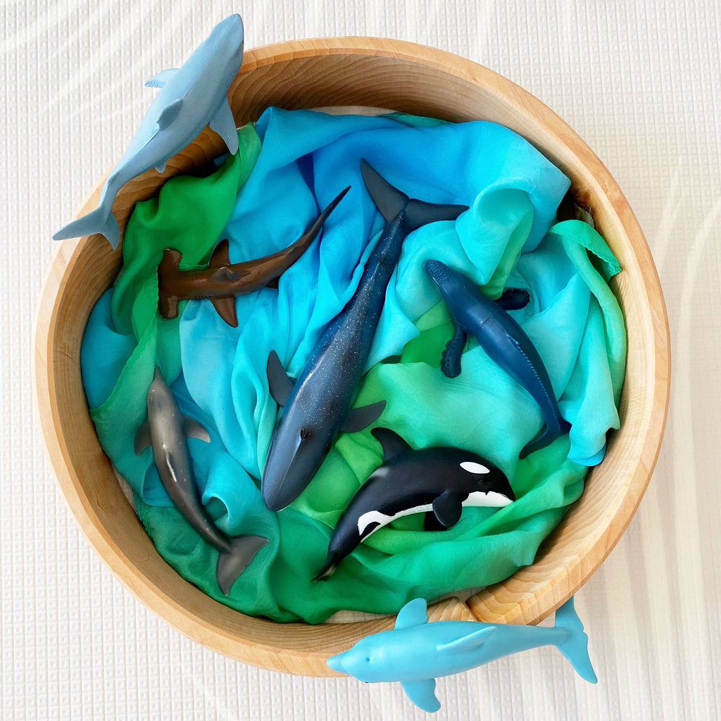 Wooden bowl filled with toy dolphins and shark figures on a textured white surface