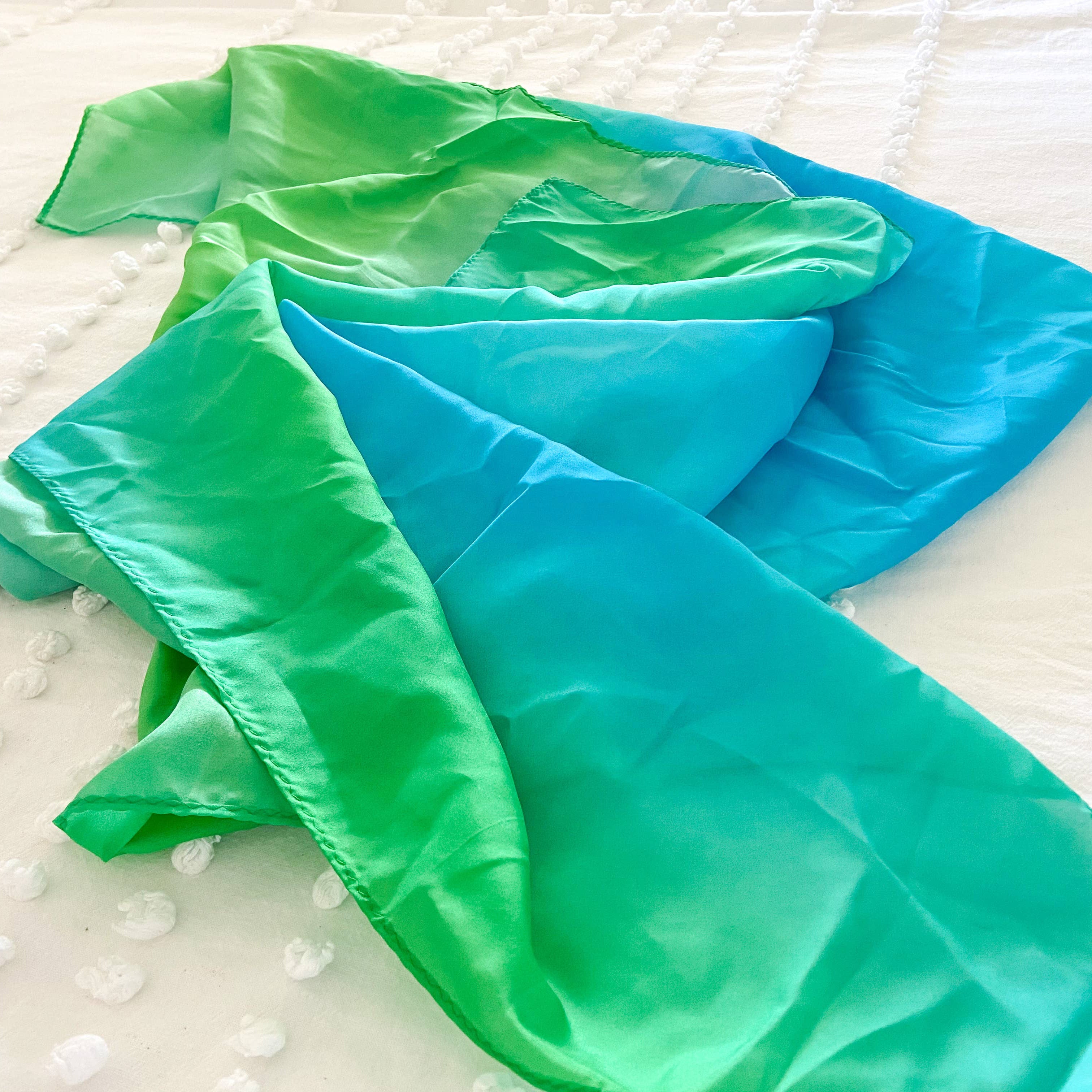 Two green and blue gradient scarves on a textured white surface