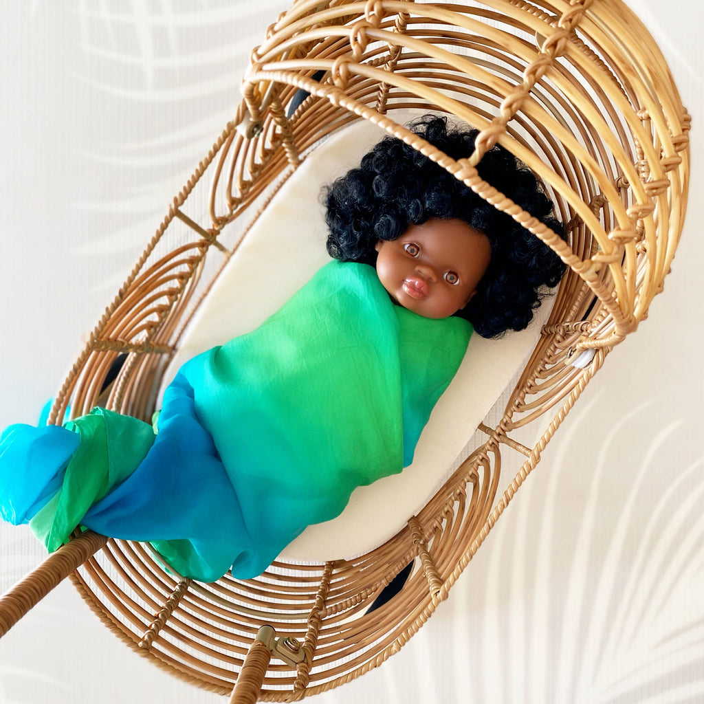 Baby doll with green wrap in a wicker basket on a white background