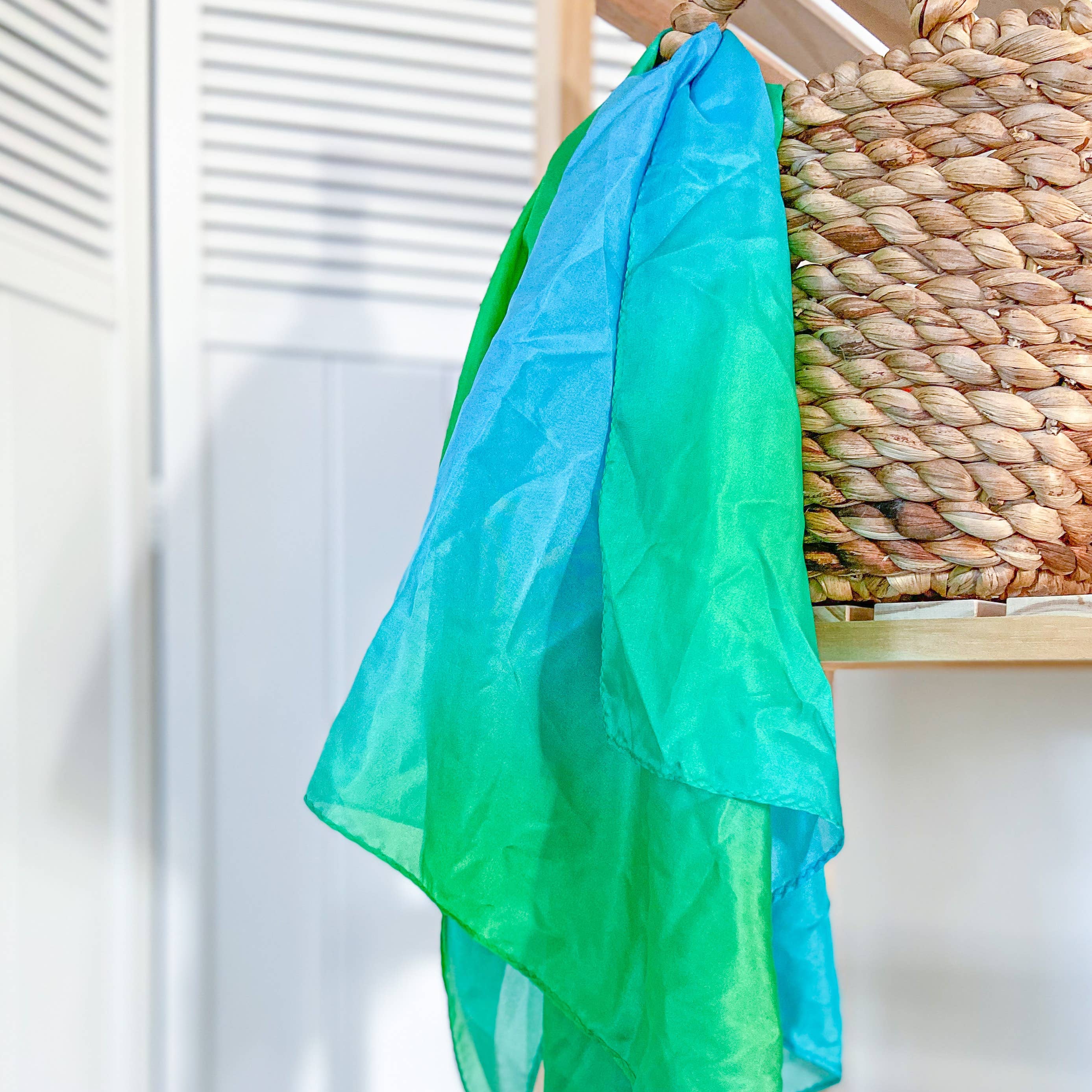 Green and blue scarf draped over a woven basket on a wooden surface.