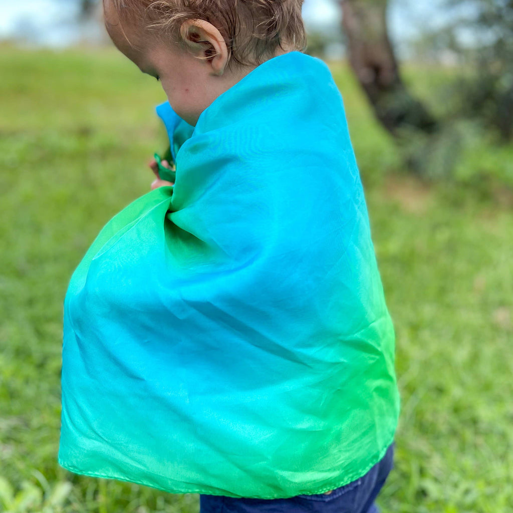 Child wearing a green and blue cape outdoors on a grassy area