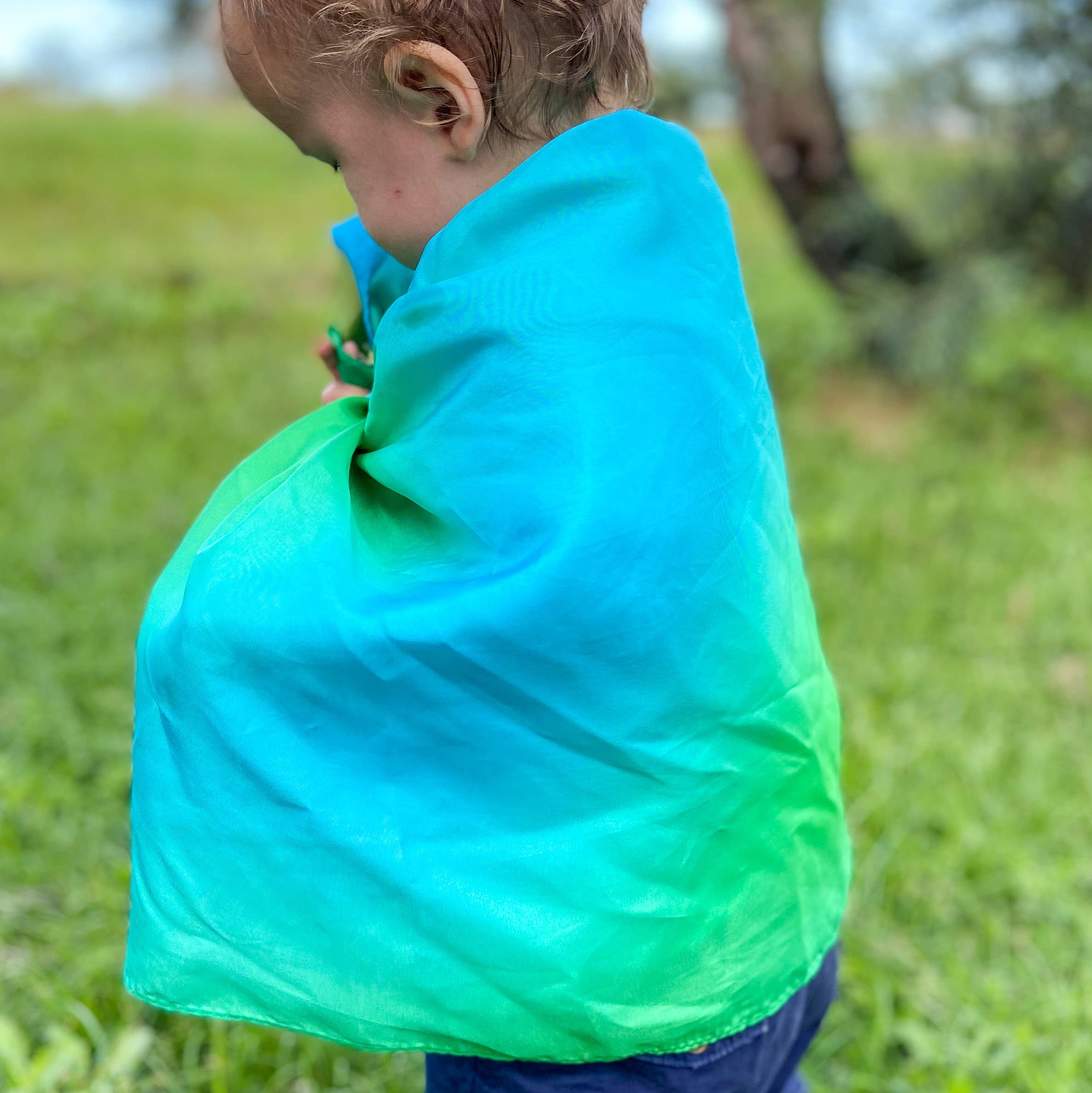 Child wearing a green and blue cape outdoors on a grassy area