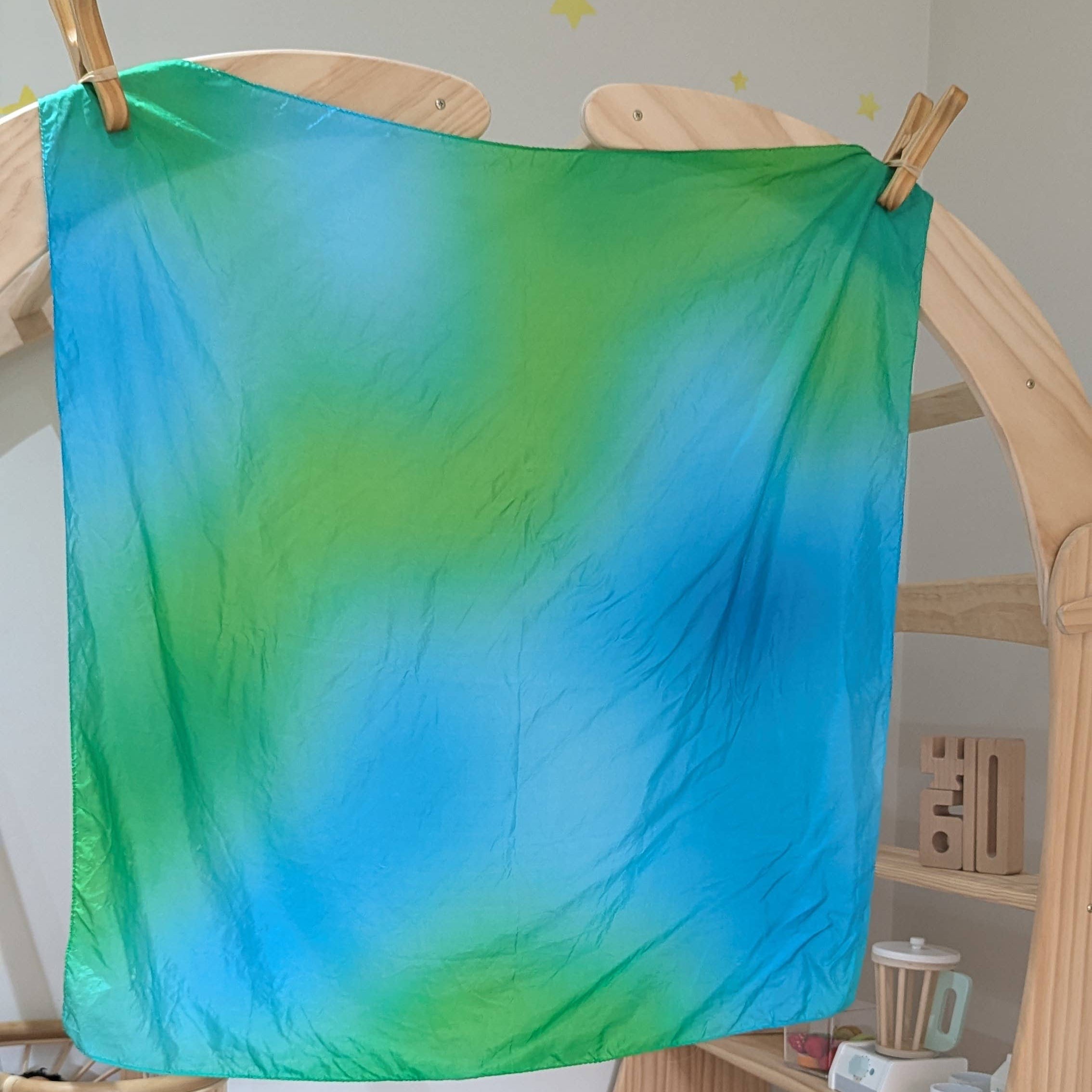 Colorful tie-dye cloth hanging on a wooden frame in a room with toys and furniture.