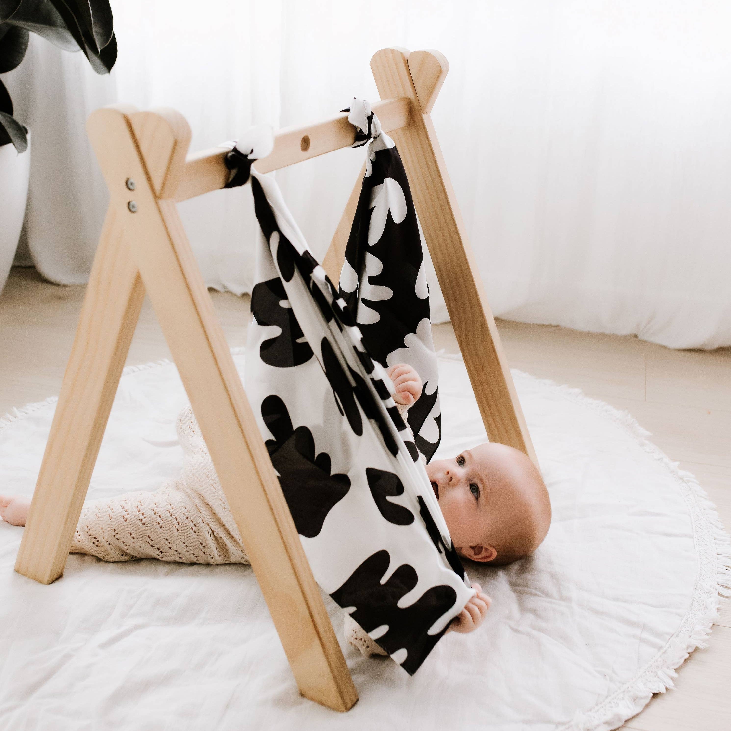 Baby lying on a wooden play gym with a black and white patterned blanket
