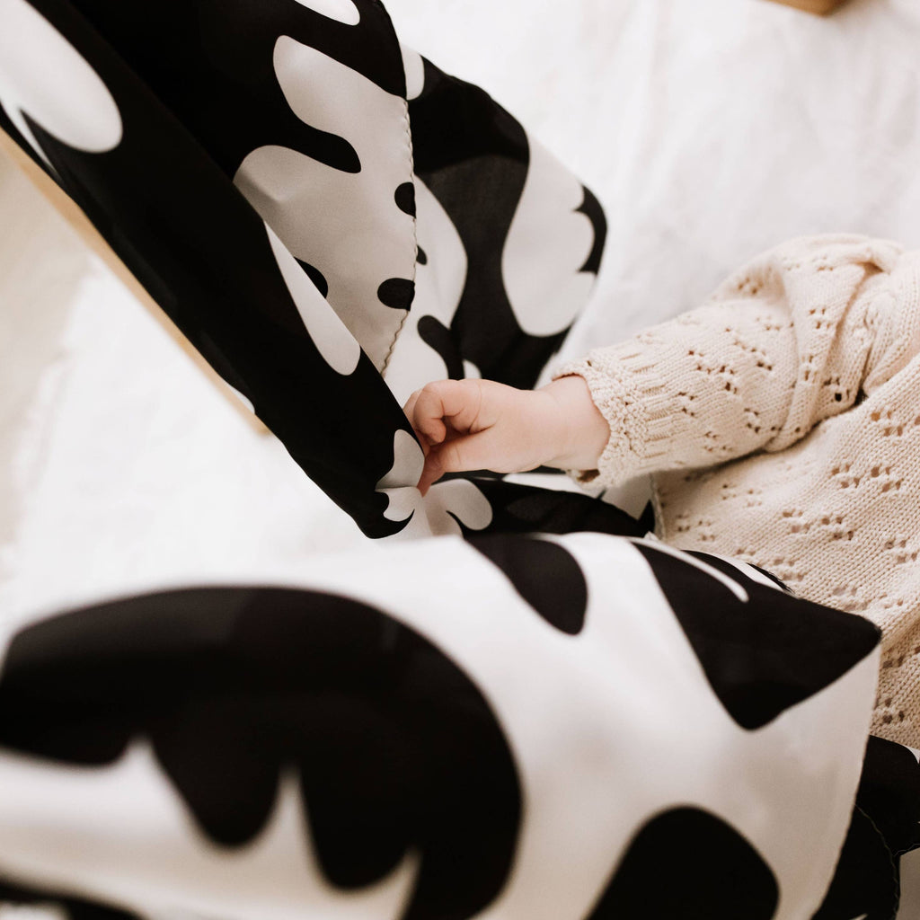 Person holding a black and white patterned blanket with a child wearing a beige knit sweater.