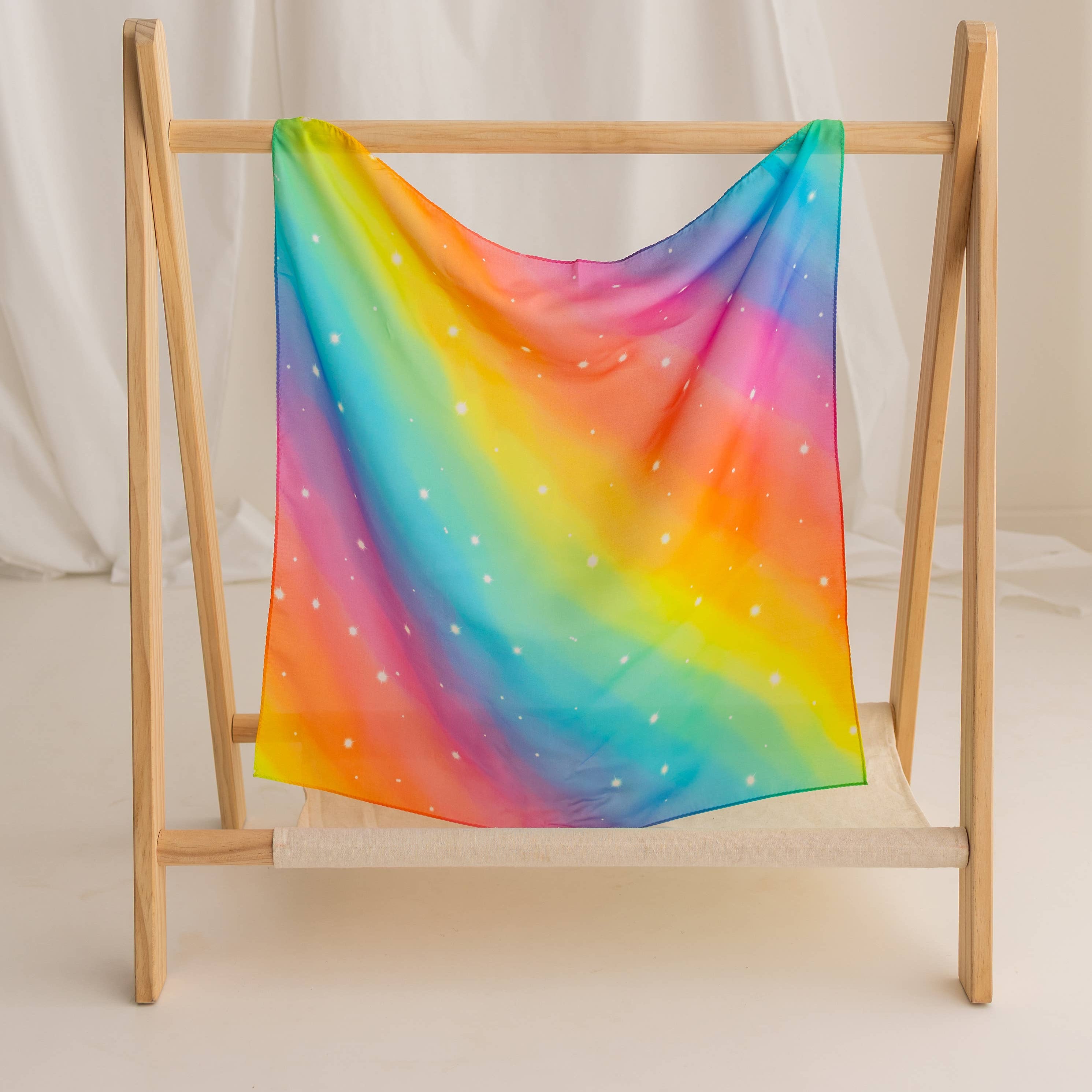Colorful rainbow-patterned towel on a wooden rack against a white curtain background
