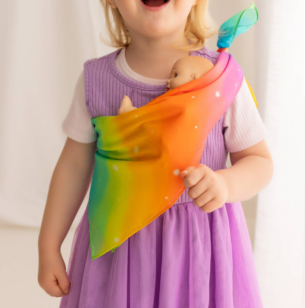 Child in a purple dress holding a colorful rainbow scarf against a white curtain background