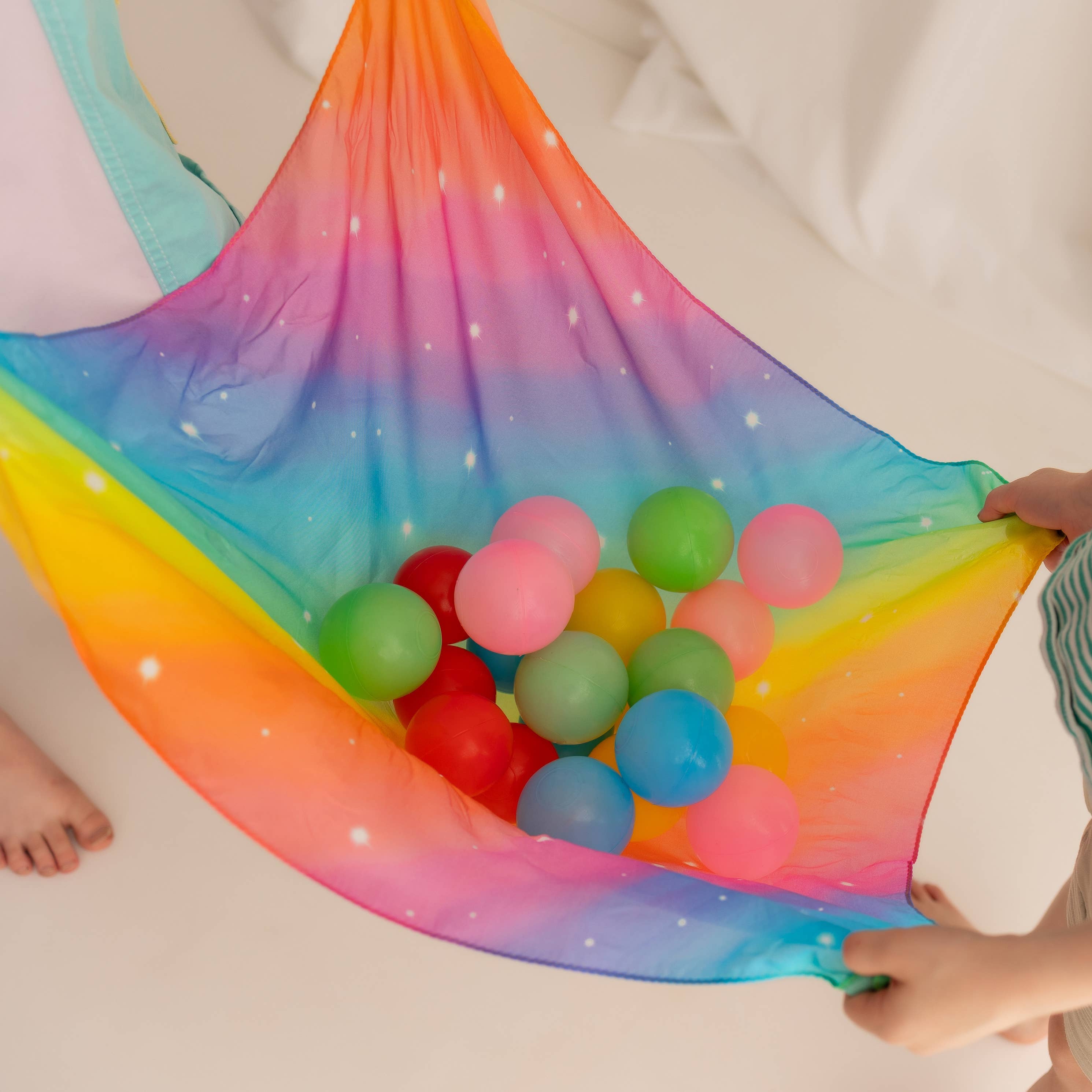 Colorful ball pit hammock with multicolored balls held by a person wearing a green and white striped shirt.