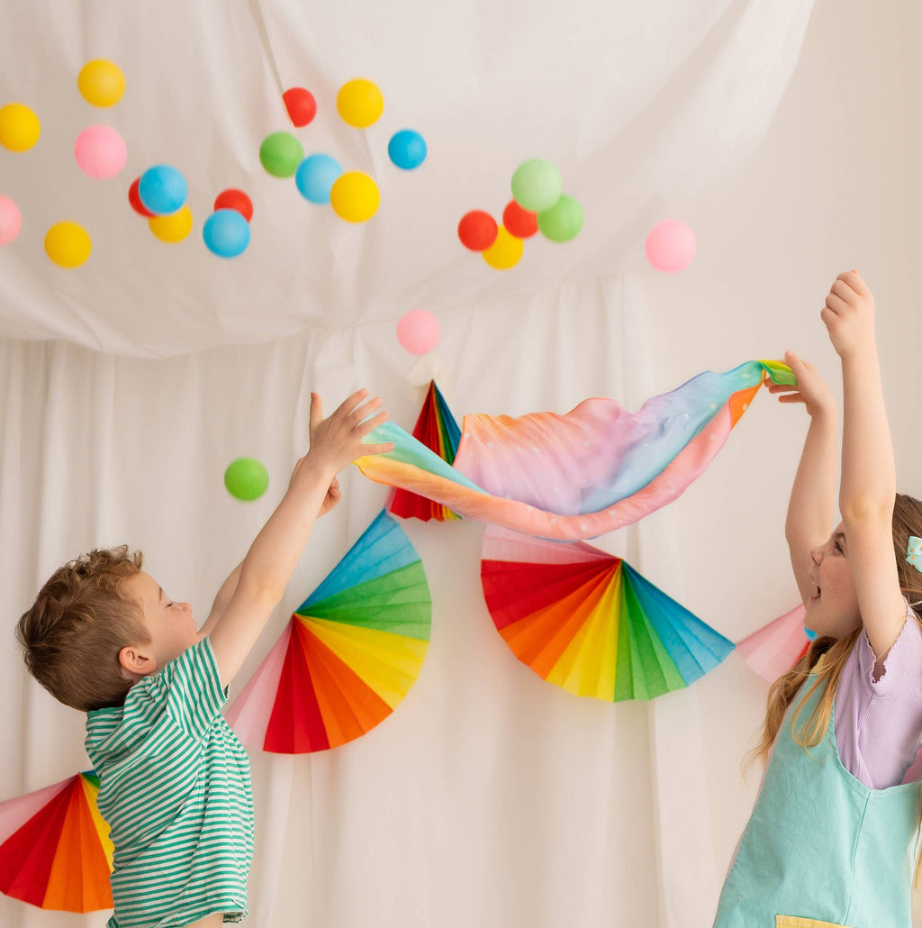Two children playing with colorful paper fans against a white backdrop