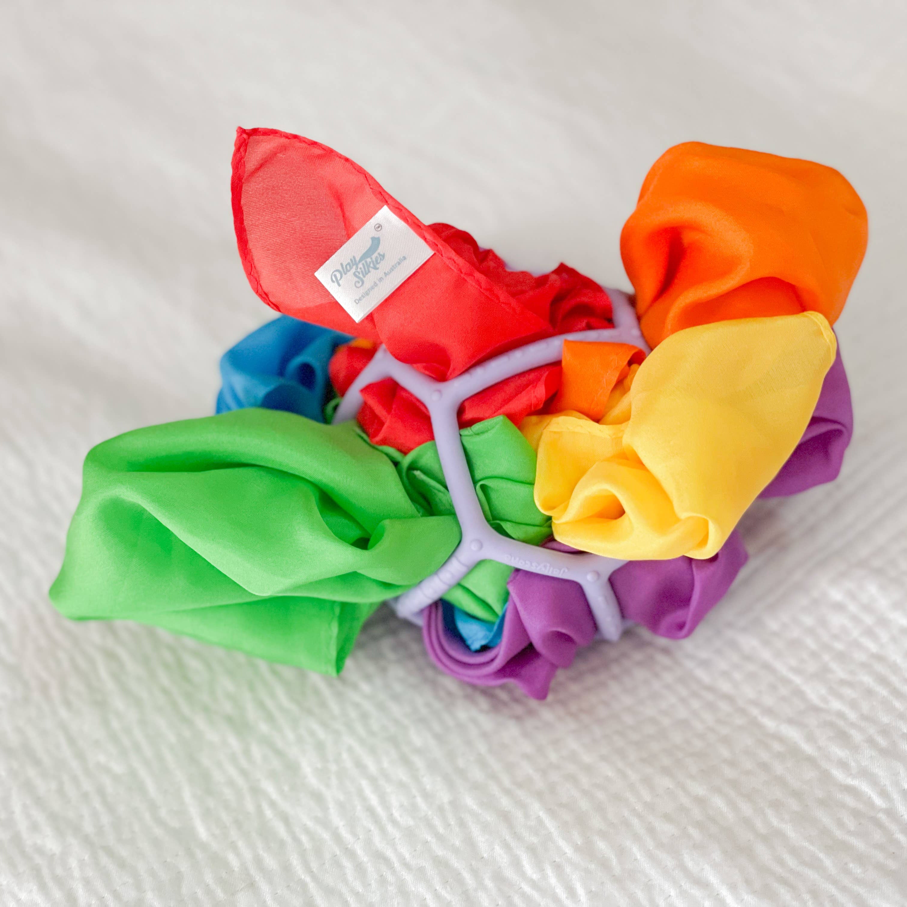 Colorful silks arranged in a circular pattern on a white fabric background