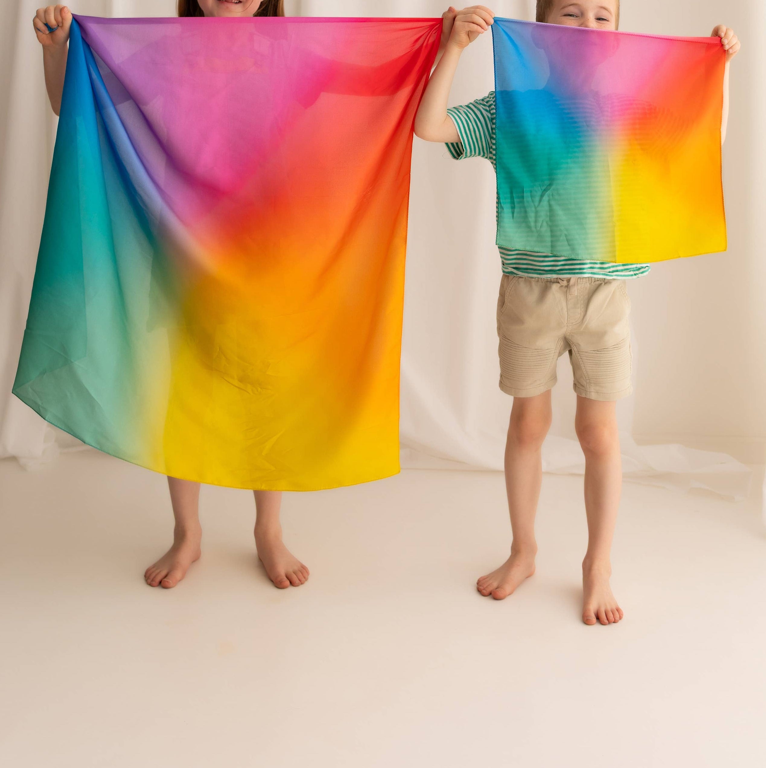 Two children holding a colorful tie-dye fabric against a white background