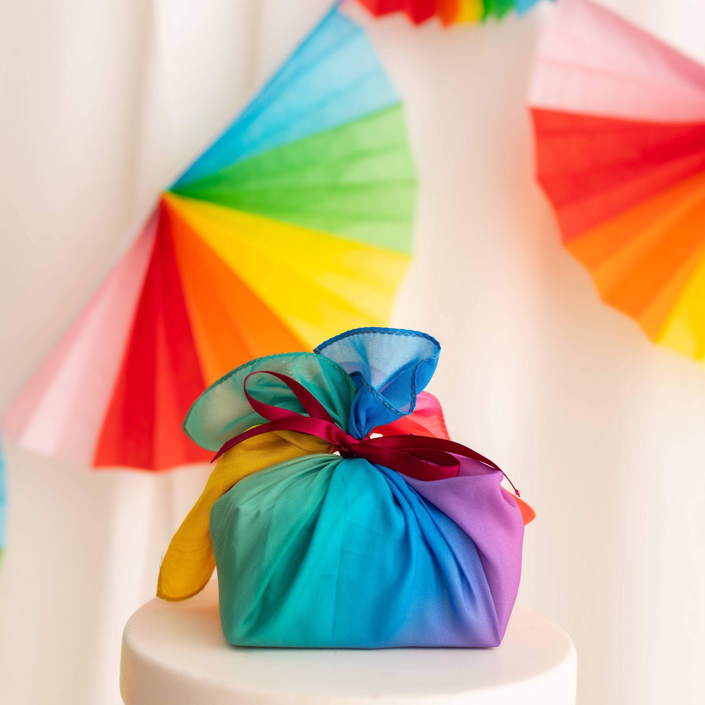 Colorful fabric bundle on a white surface with rainbow-colored fans in the background