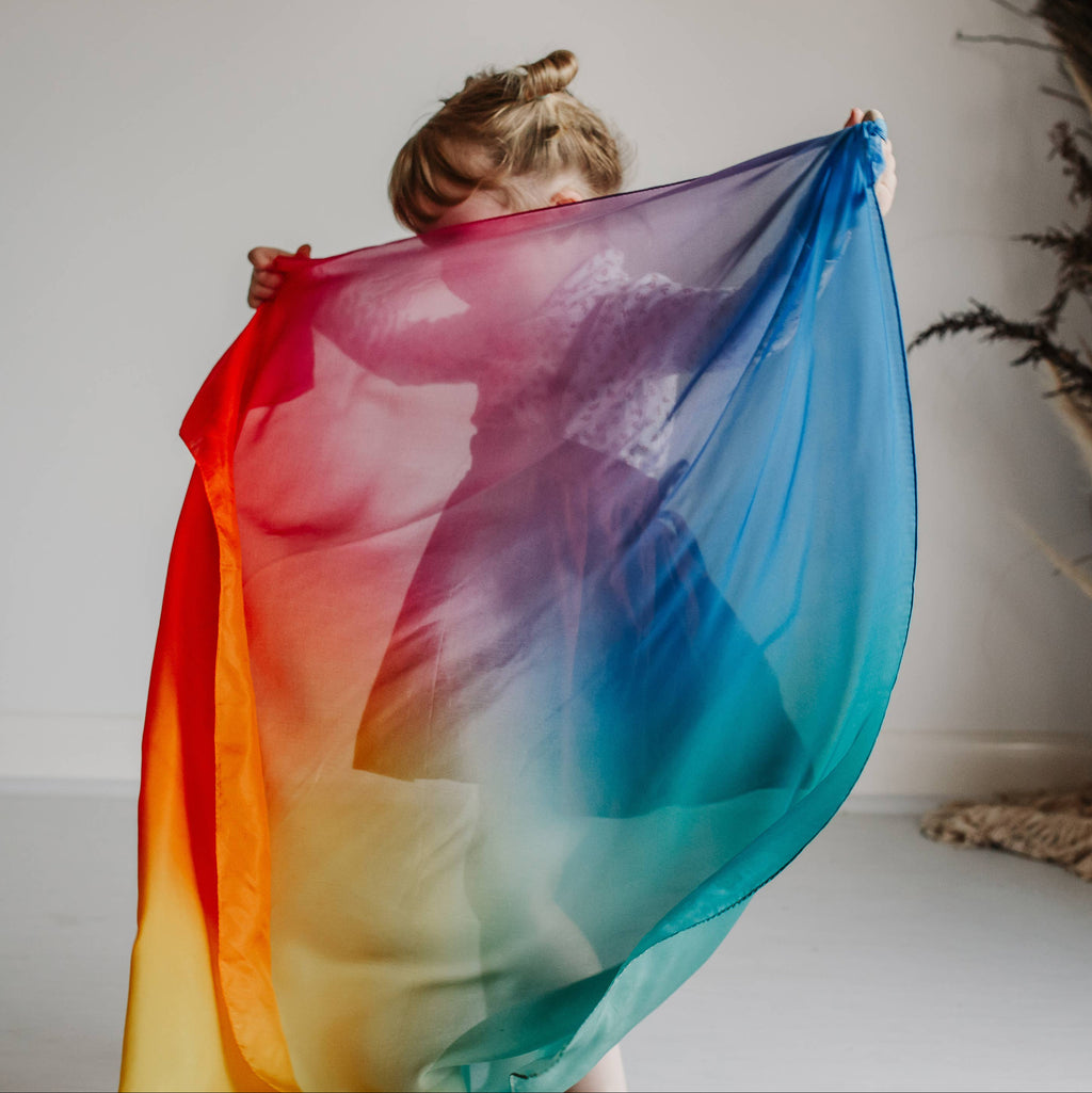 Person holding a colorful scarf in front of a white wall with decorative elements.