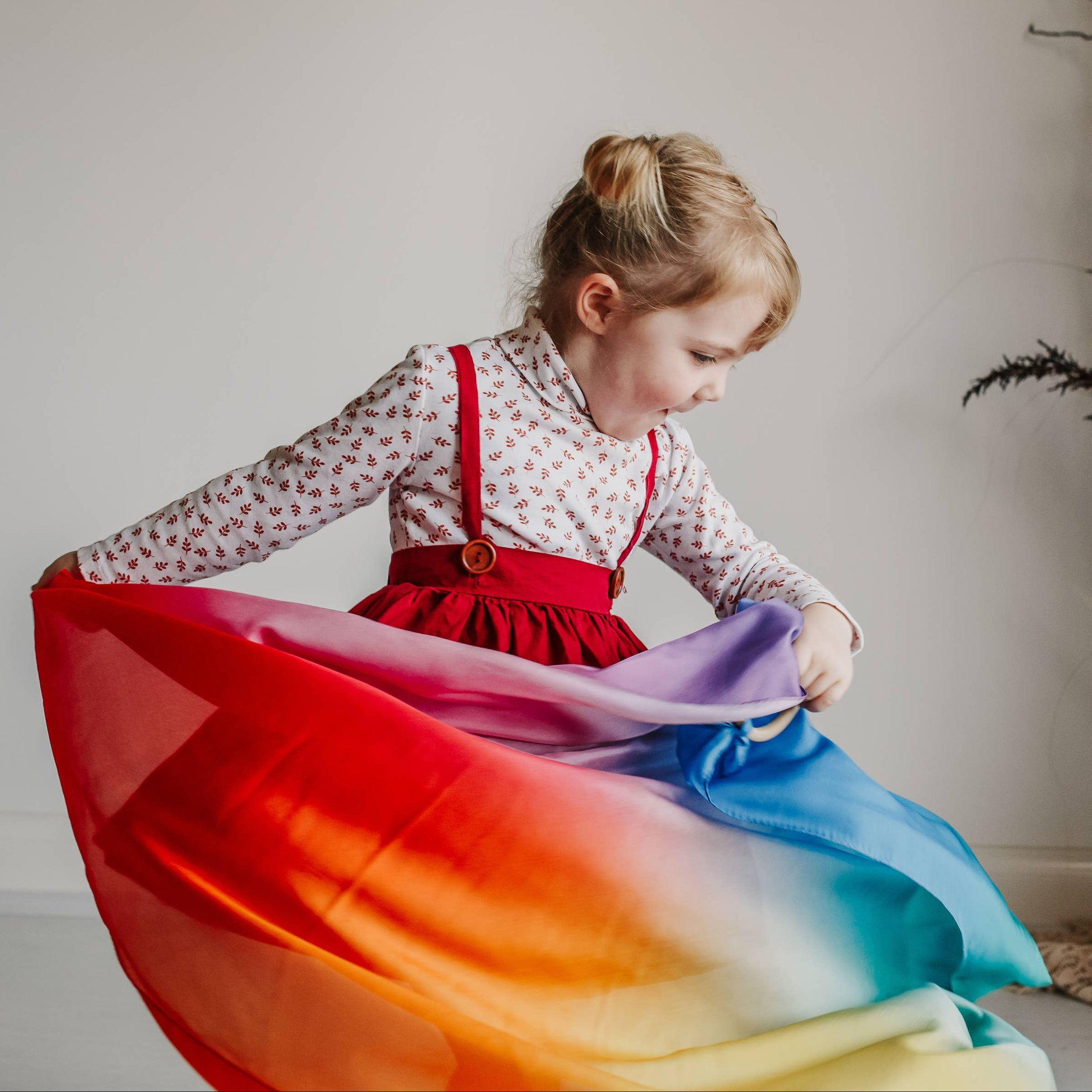Child holding a colorful scarf in a room with a neutral background