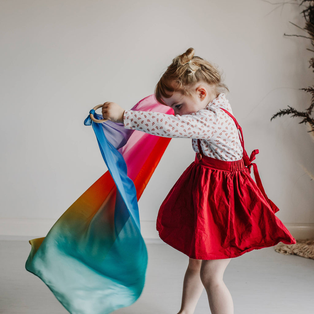 Child in a red dress holding a colorful scarf in a room with decorative elements.