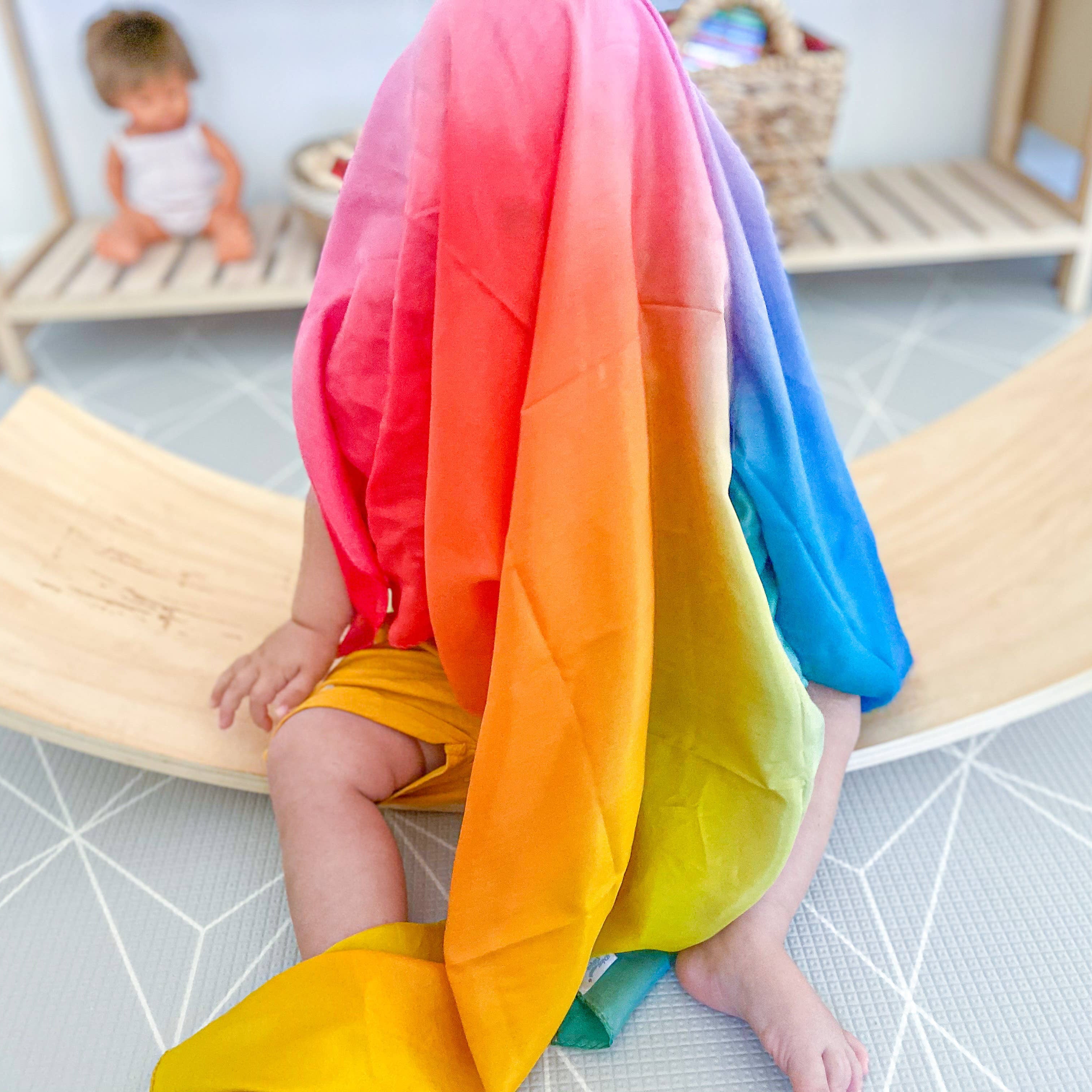 Child wearing a colorful rainbow dress sitting on a wooden chair in a room.