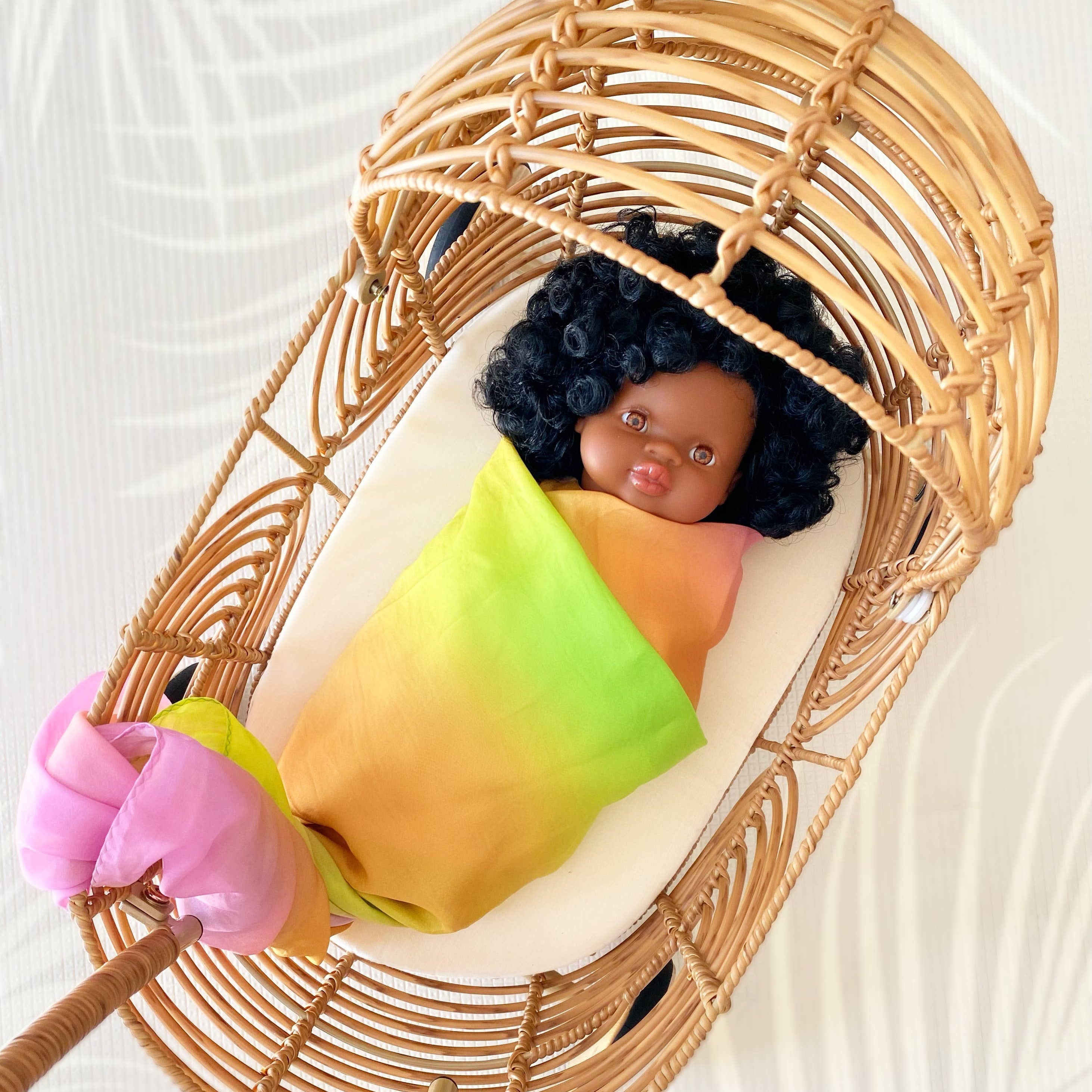 Baby doll wrapped in a colorful blanket, lying in a wicker crib on a textured white background