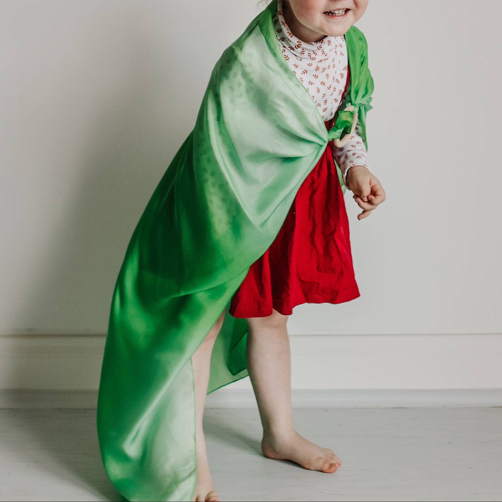 Child in a green and red outfit standing against a plain wall with decorative elements.