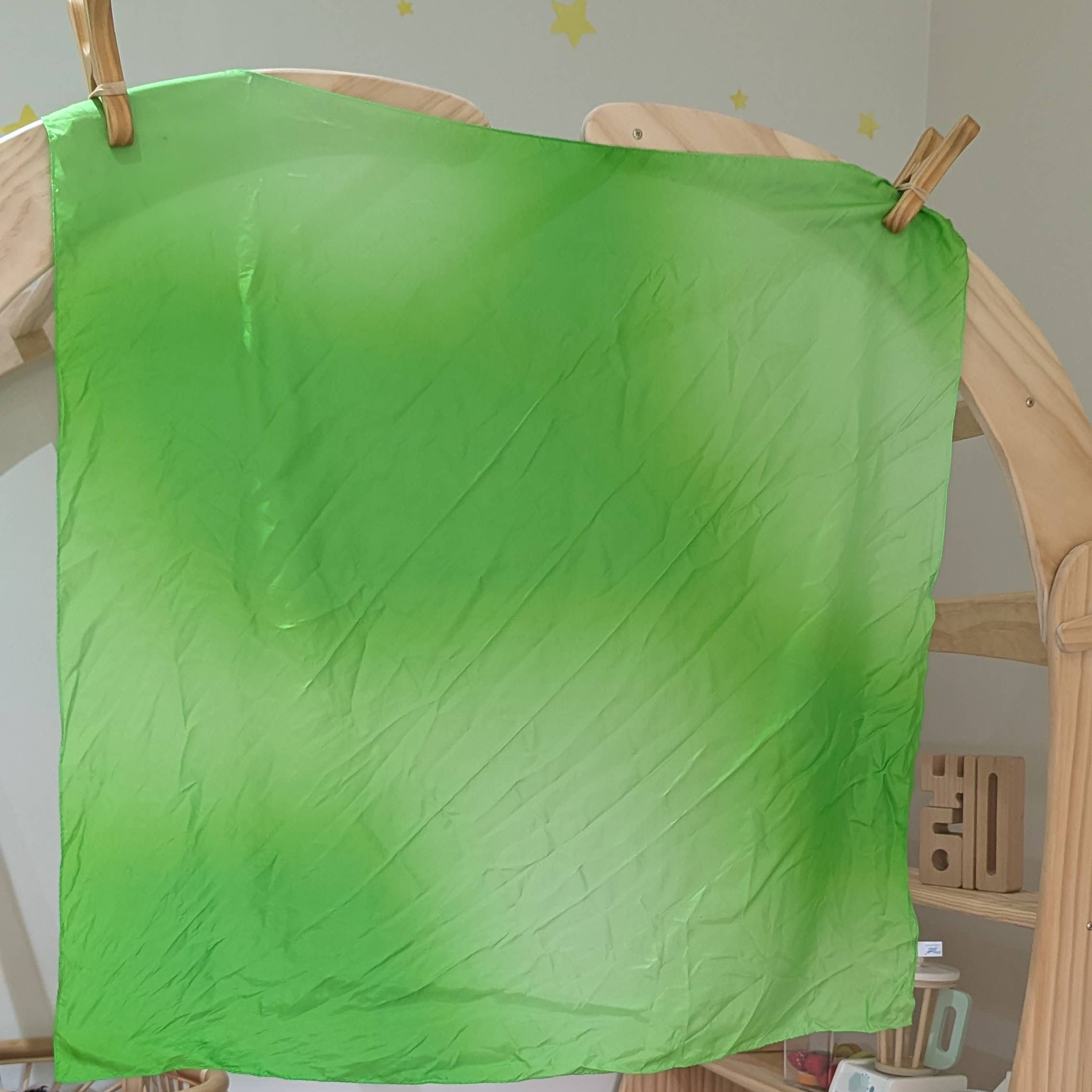 Green fabric on a wooden frame with toys and a chair in the background