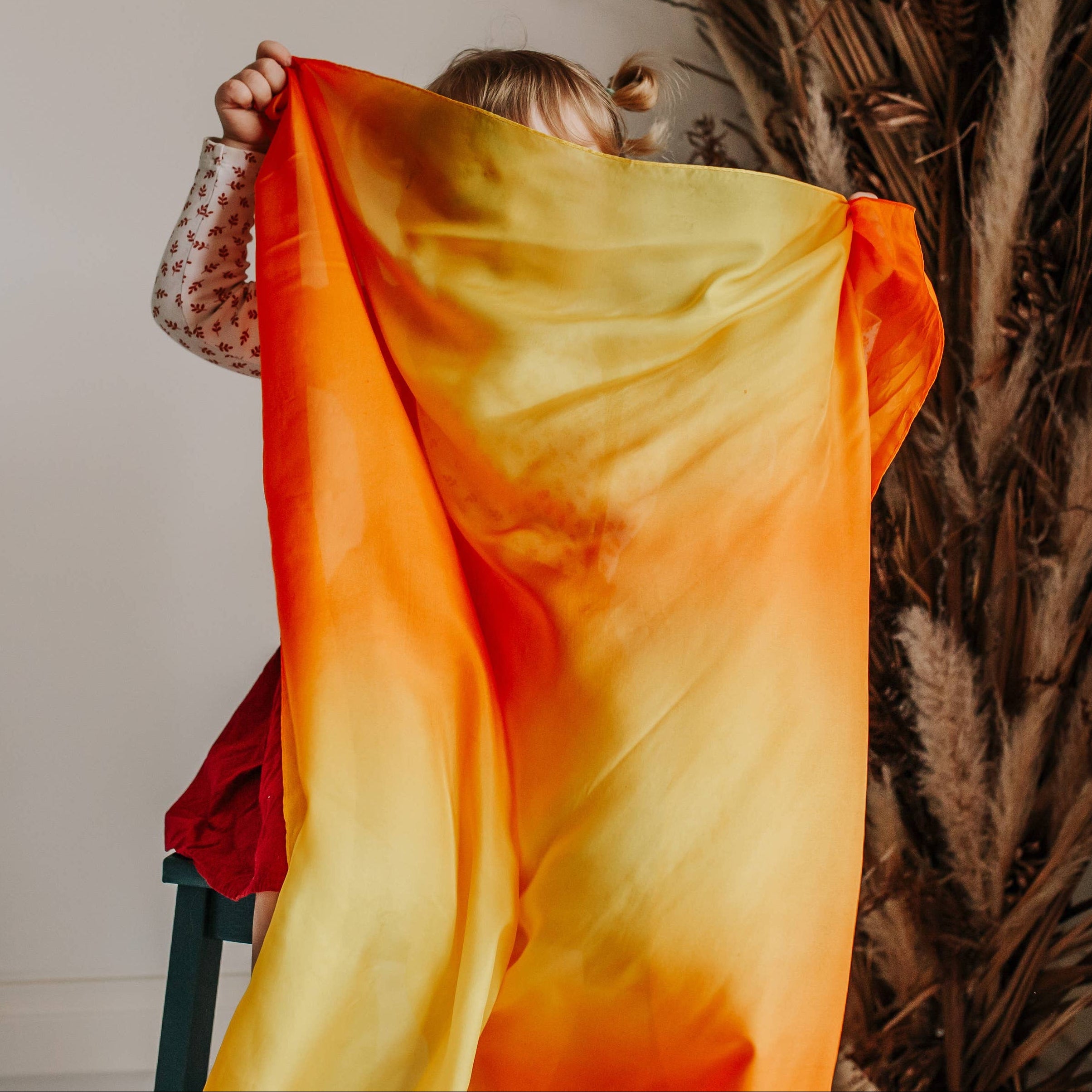 Person holding a vibrant orange and yellow fabric in front of a neutral background with decorative elements.