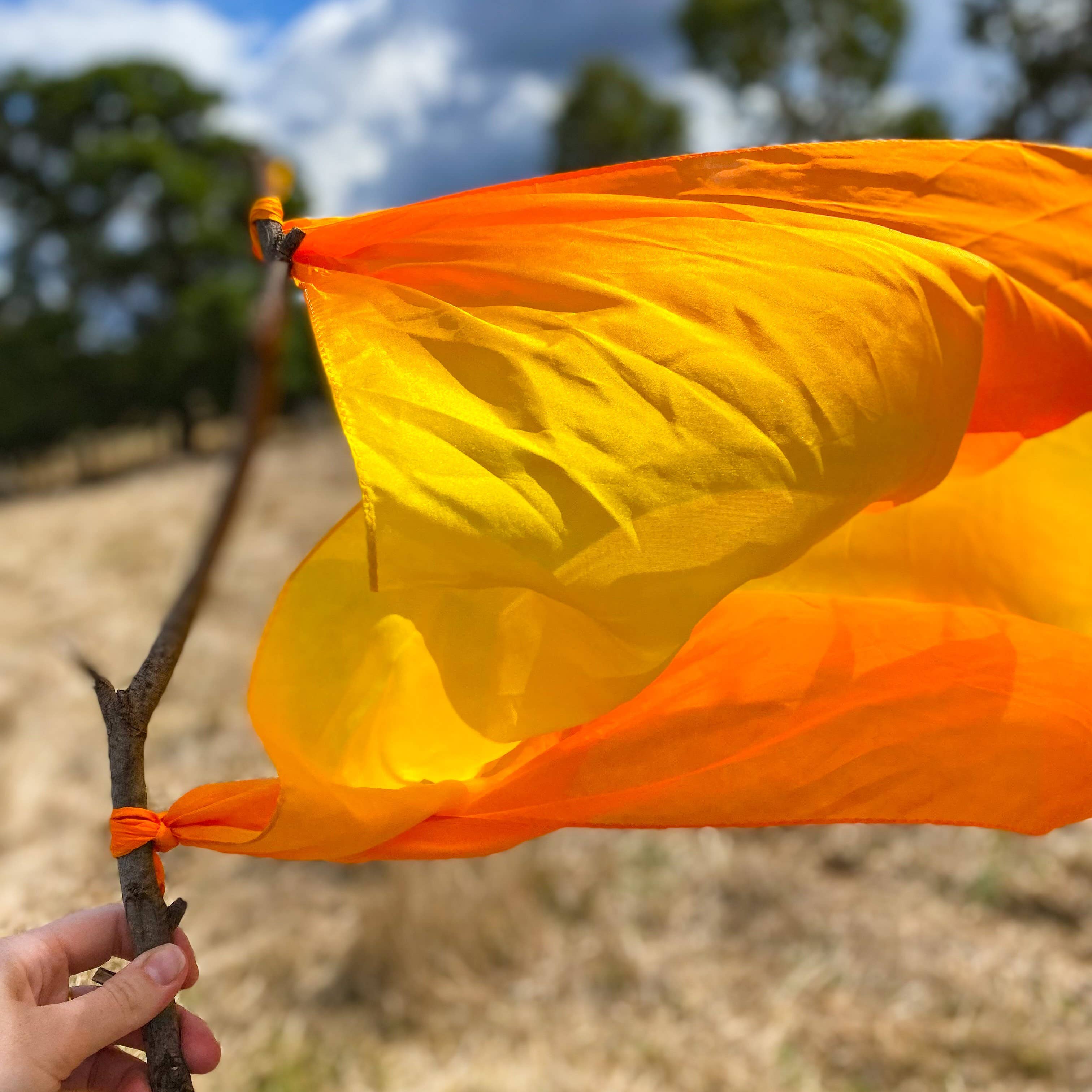 Orange silk flag held by a hand with a blurred natural background