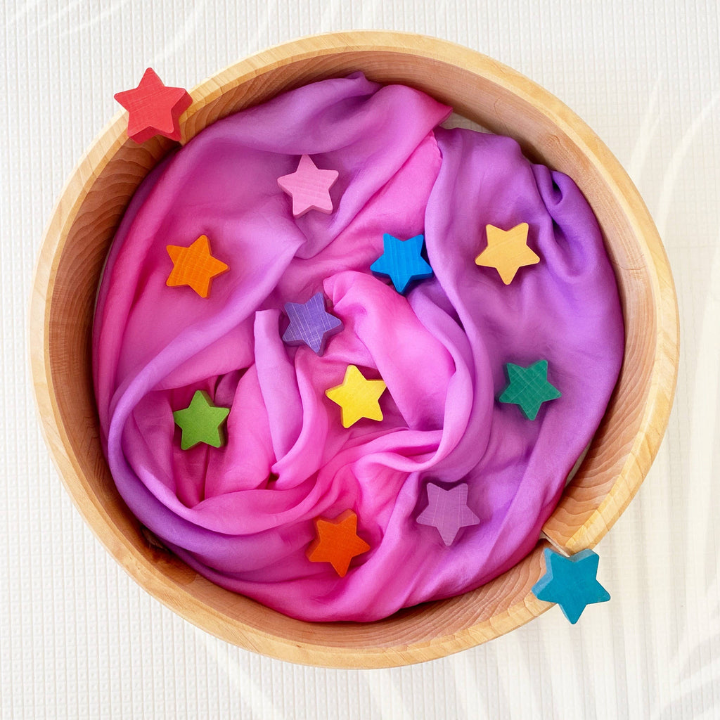 Pink play silk with colorful star-shaped decorations in a wooden bowl on a white background