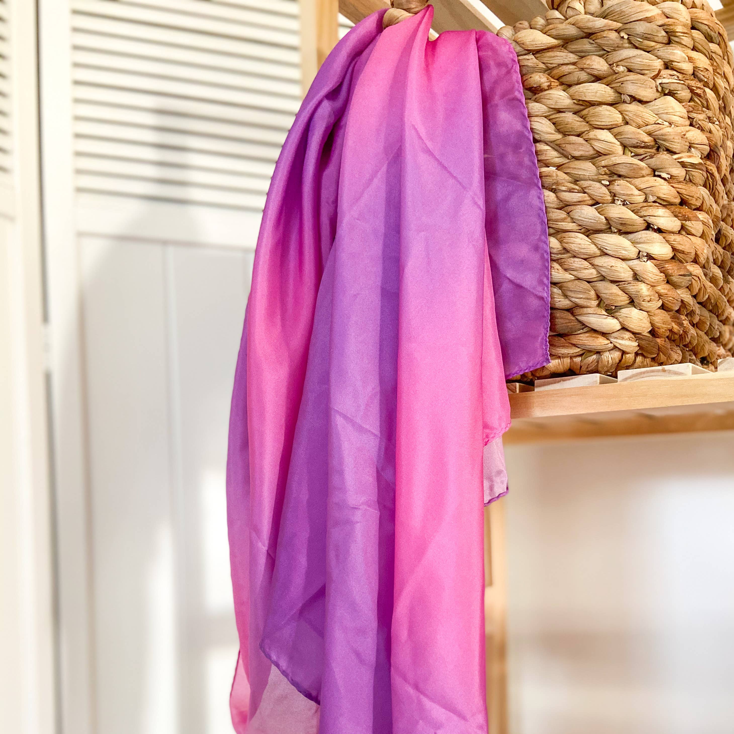 Gradient pink to purple silk hanging on a wooden chair with a woven basket in the background.