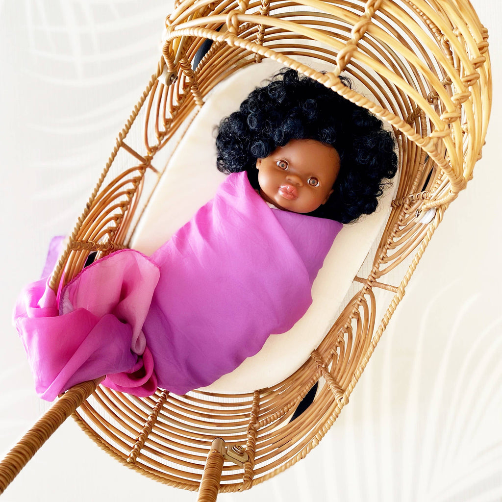 Baby doll wrapped in pink cloth lying in a wicker basket on a white background