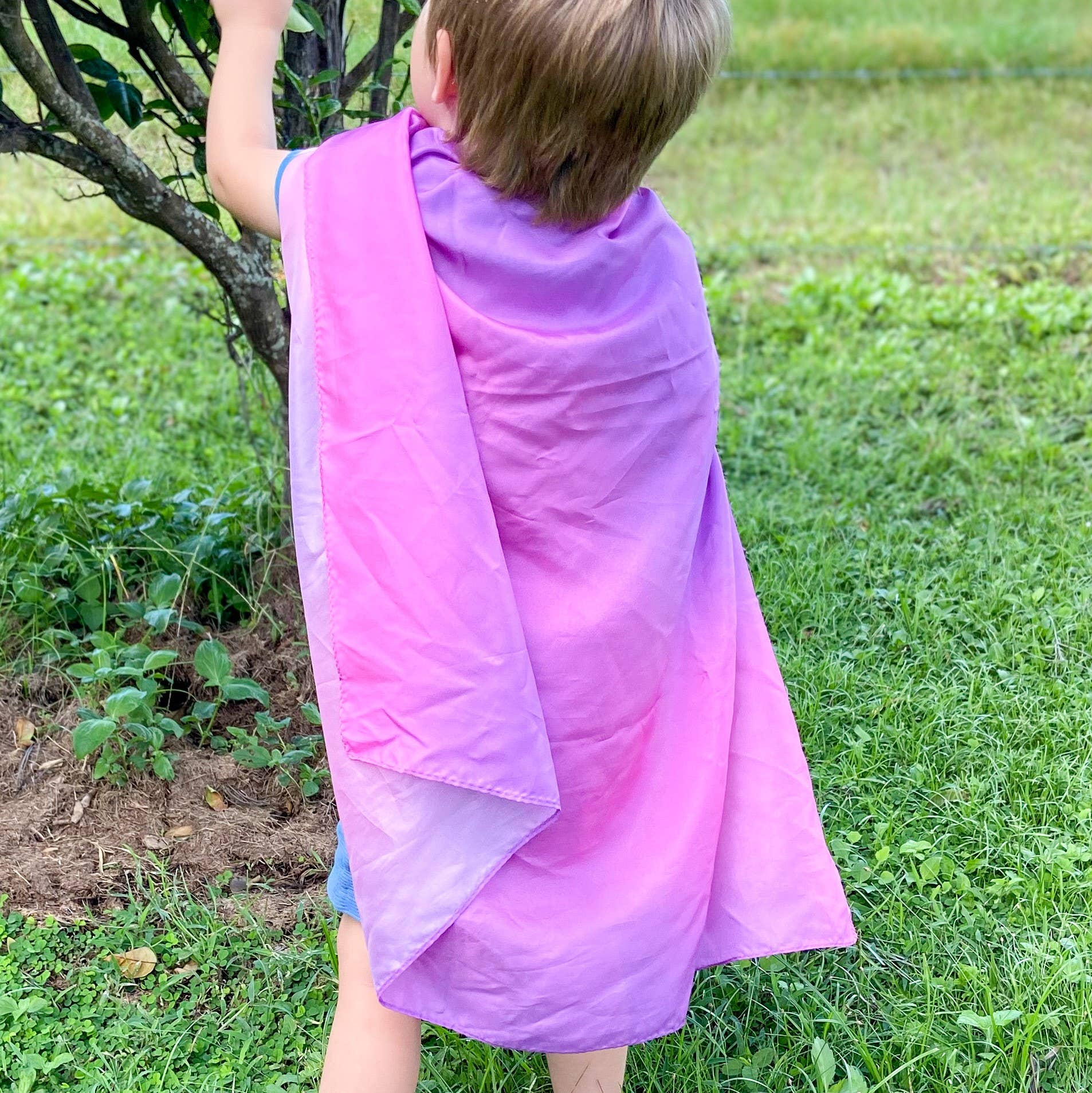 Child wearing a purple play silk outdoors on grass