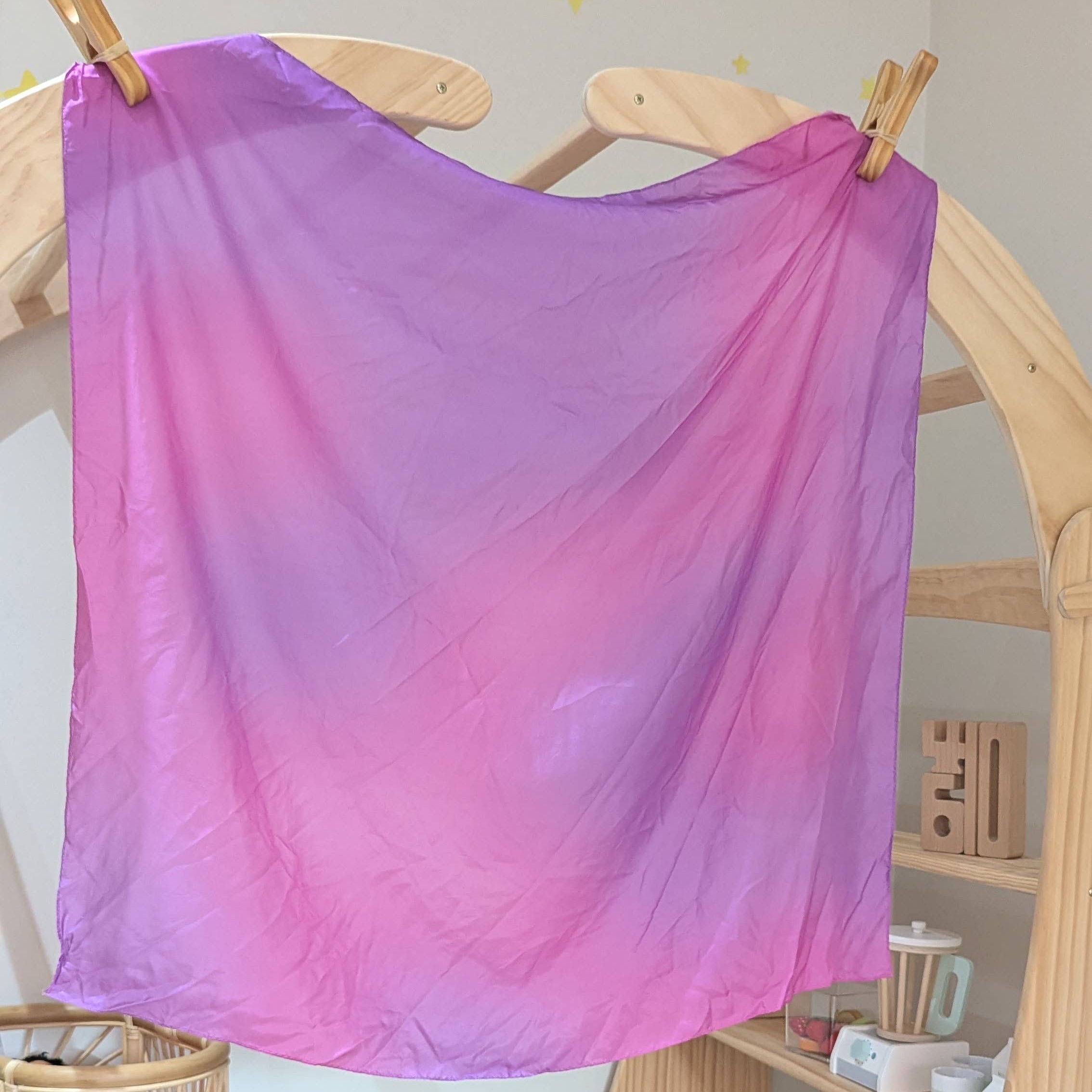 Gradient purple and pink fabric hanging on a wooden rack in a room with toys and furniture.