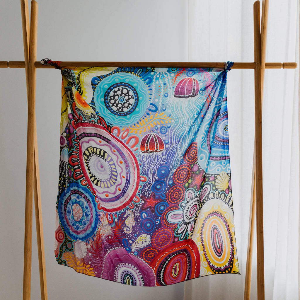 Colorful silk with intricate patterns hanging on a wooden rack against a white curtain.