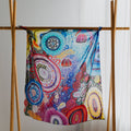 Colorful silk with intricate patterns hanging on a wooden rack against a white curtain.