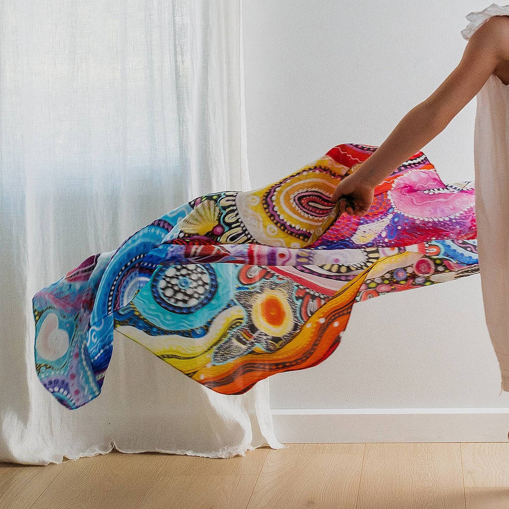 Young girl in a white dress holding a colorful dress against a white curtain backdrop