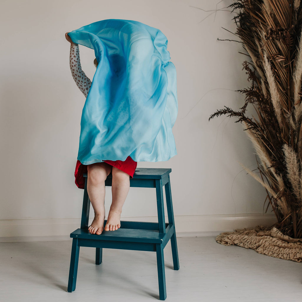 Person wrapped in a blue towel on a stool against a neutral wall with decorative elements.