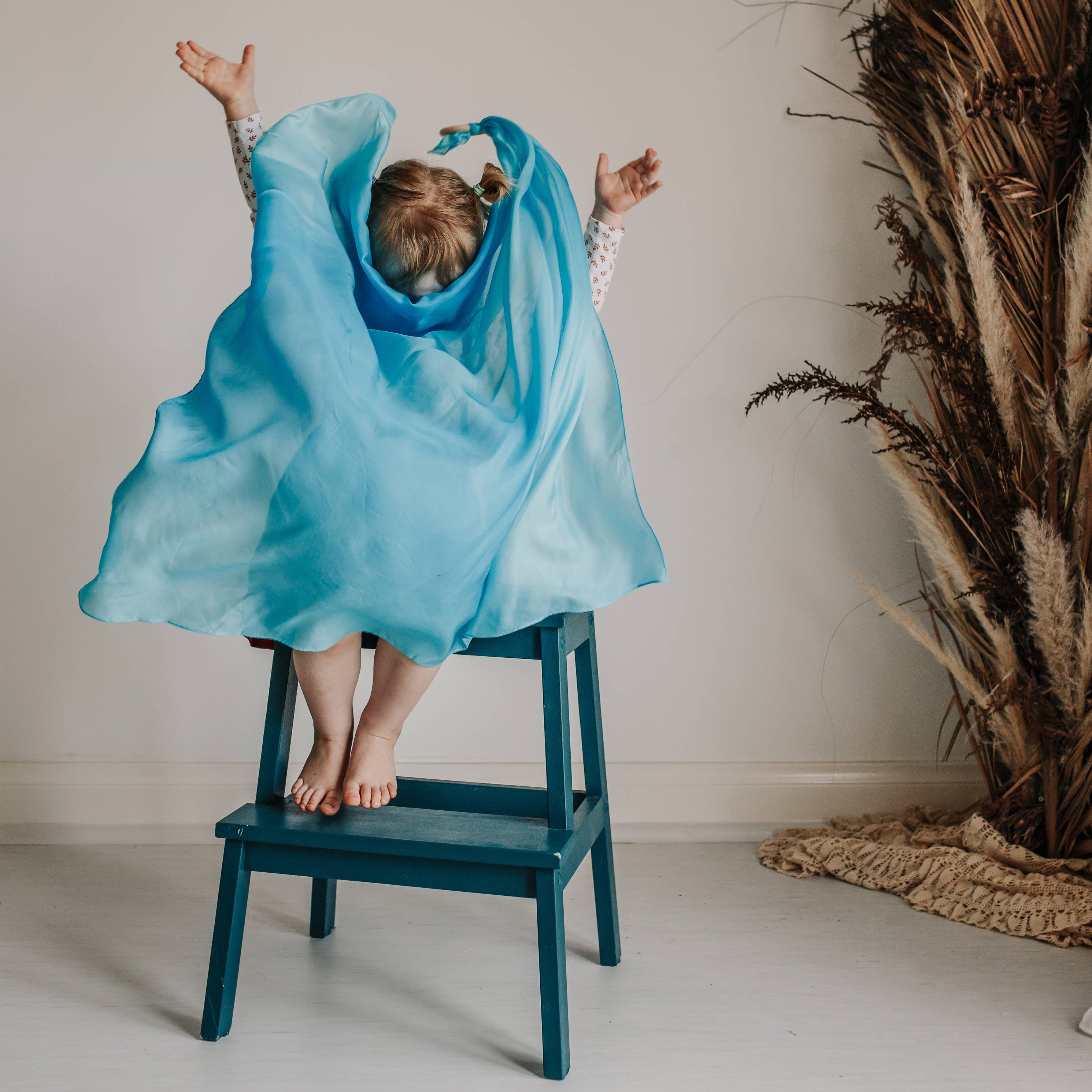Child in a blue dress standing on a chair with a neutral background