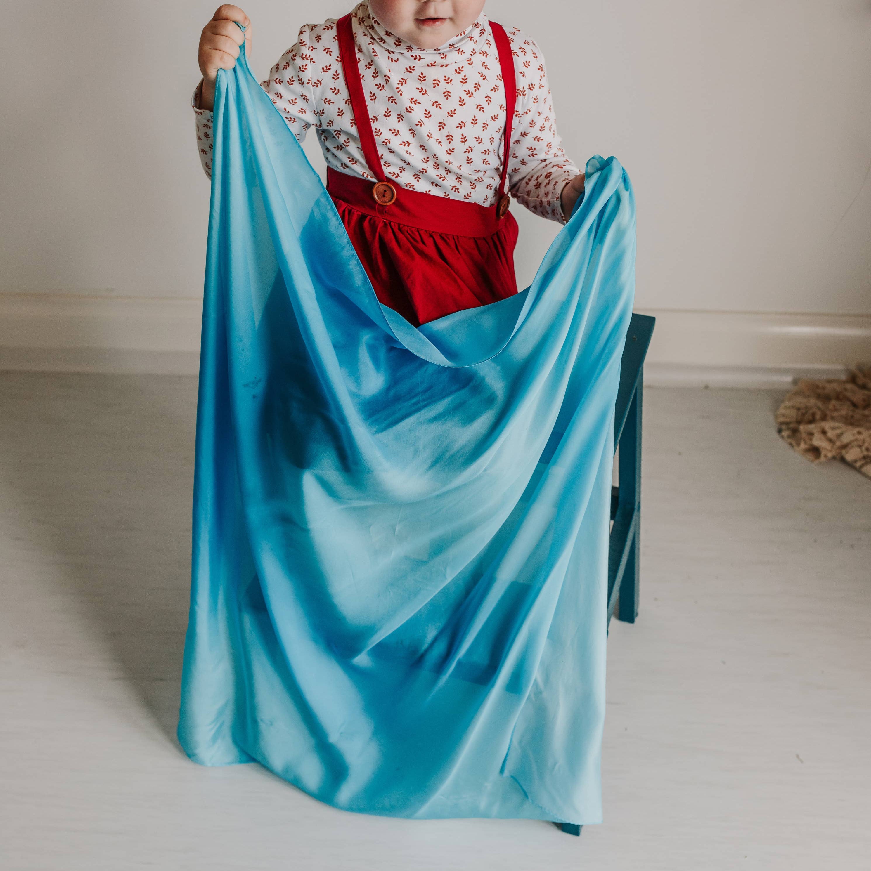 Child holding a blue fabric in a minimal indoor setting