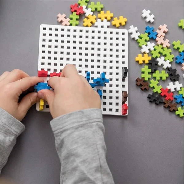 Child's hands assembling colorful puzzle pieces on a grid board with a blue case in the background.