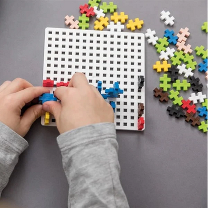 Child's hands assembling colorful puzzle pieces on a grid board with a blue case in the background.