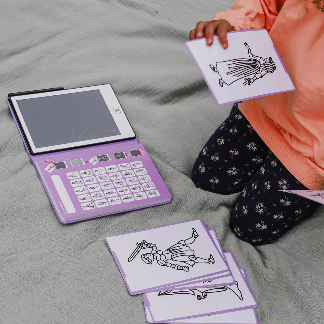 Person holding a card with a drawing of a character next to an open purple electronic device on a bed.