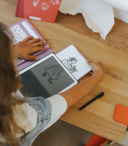 Person using a digital drawing tablet on a wooden table with a pen and paper.