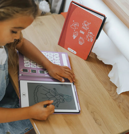 Child using a tablet with a stylus on a wooden table, next to a red book.