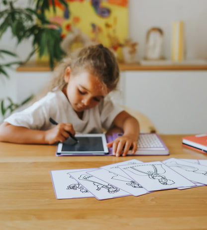 Child drawing on a tablet with coloring sheets on a table