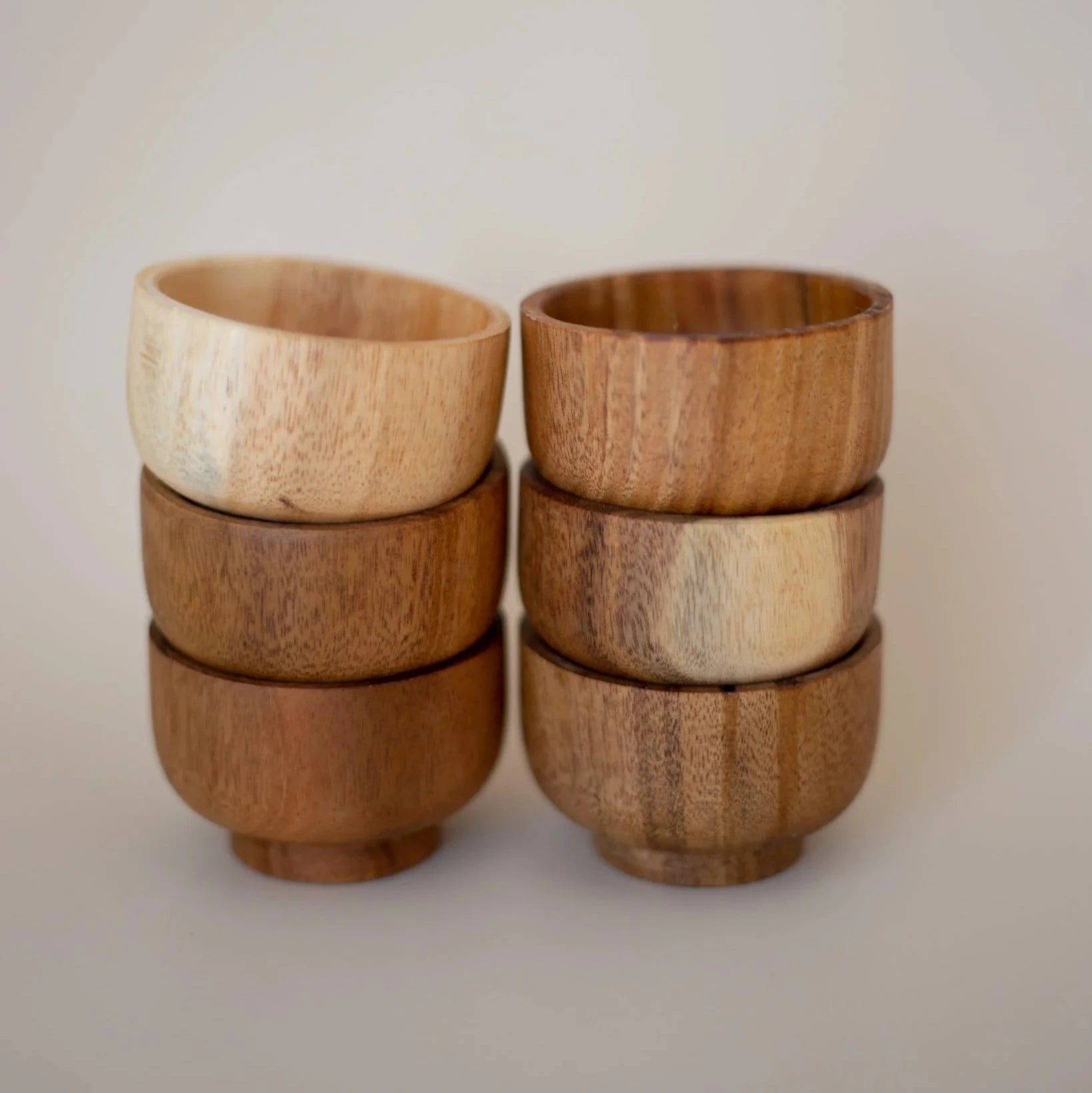 A set of six stacked mini wooden bowls with varying shades and grain patterns.