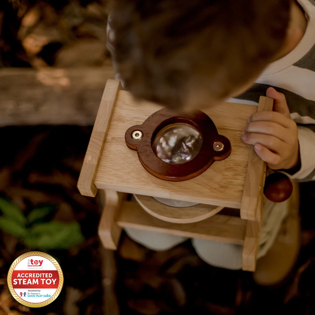 Child playing with a wooden toy kitchen set in a forest setting.